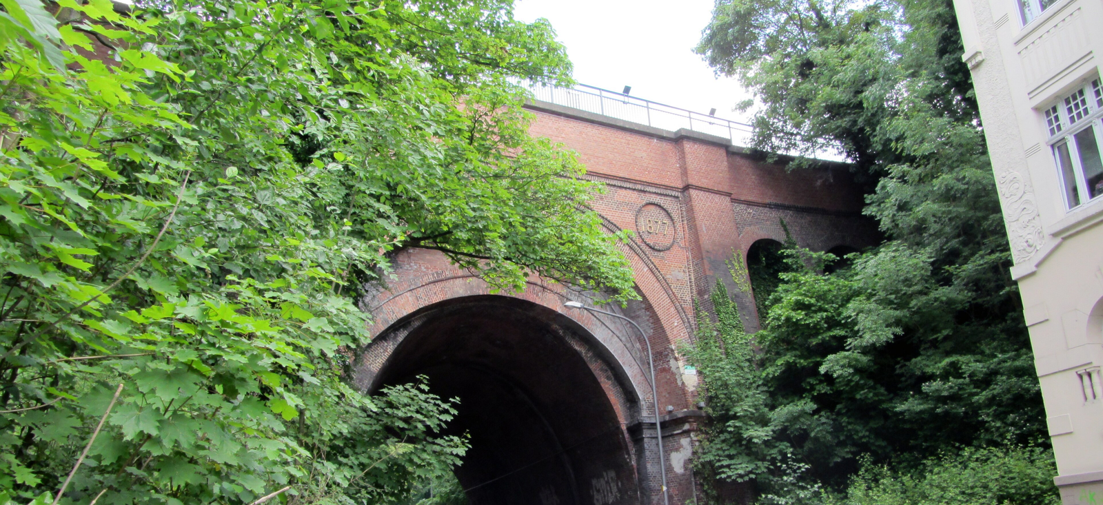 Backsteinviadukt der Nordbahntrasse von 1877 über einer Straße, umgeben von Bäumen