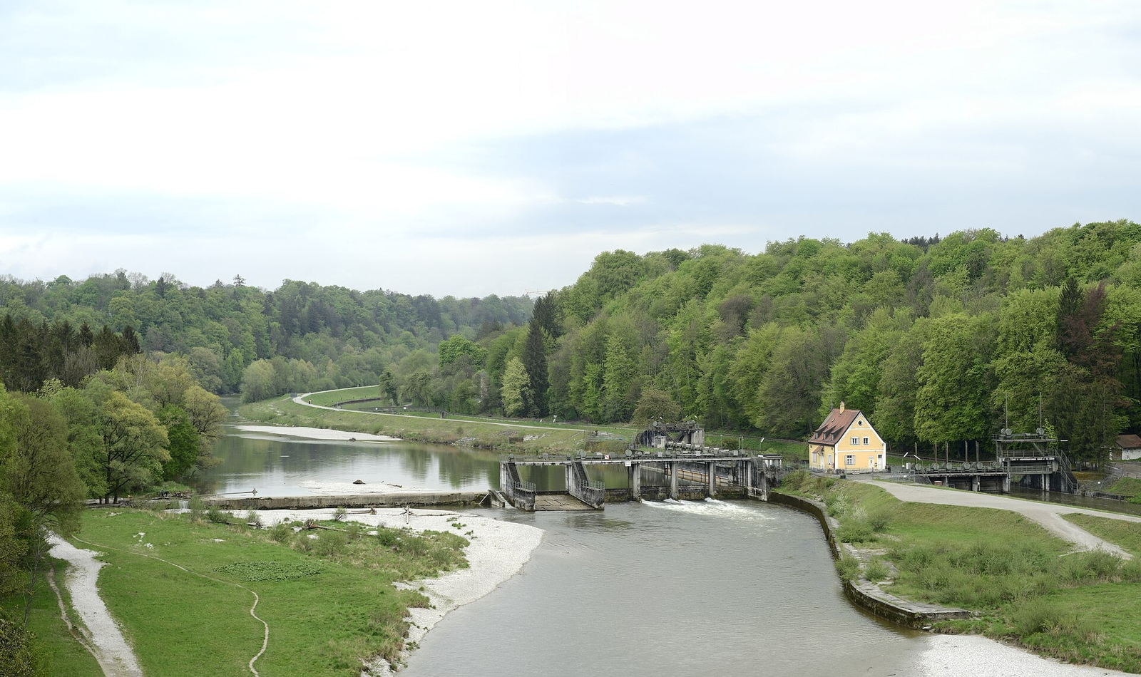 Blick von der Großhesseloher Brücke nach Süden auf die Isar mit Stauwehr und gelbem Wehrhaus, Kiesbänken, Wiesen, einem Uferweg und bewaldeten Talhängen