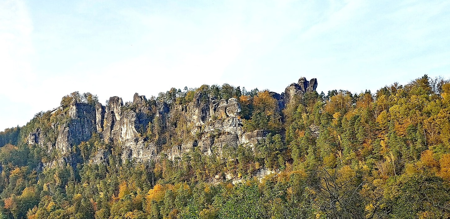 Die Felstürme der Bastei über gelb und orange gefärbtem Herbstwald, von unten aus Kurort Rathen gesehen