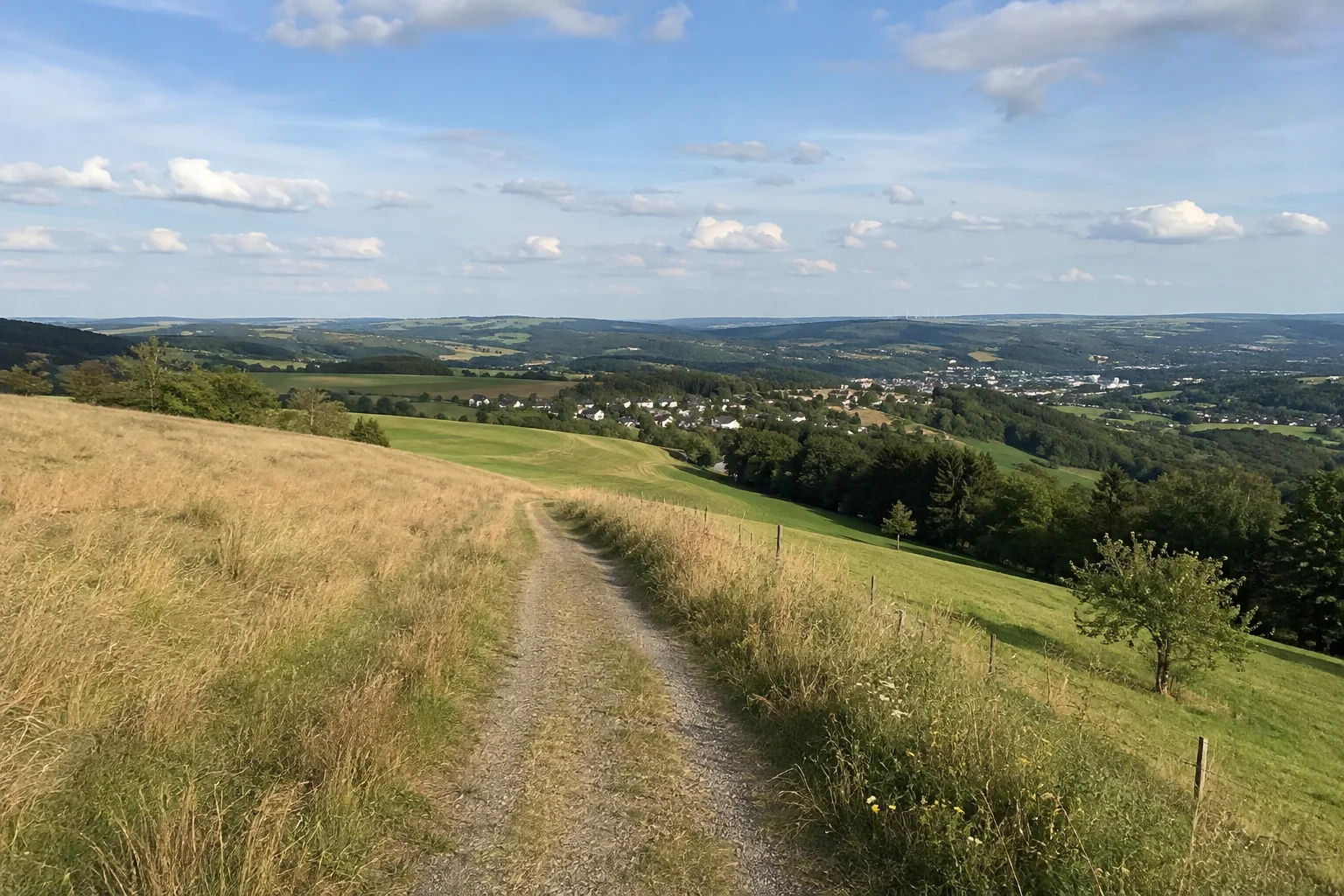 Alberodaer Höhe: offener Feldweg mit Wiesen und entfernten Häusern über einem hügeligen Talraum