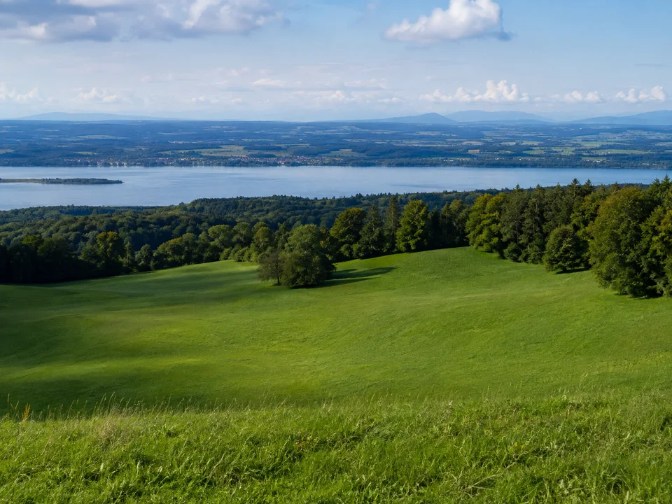 Aufkirchener Höhen: wellige grüne Wiesen oberhalb des Starnberger Sees mit Waldsaum und weitem Voralpenlandblick