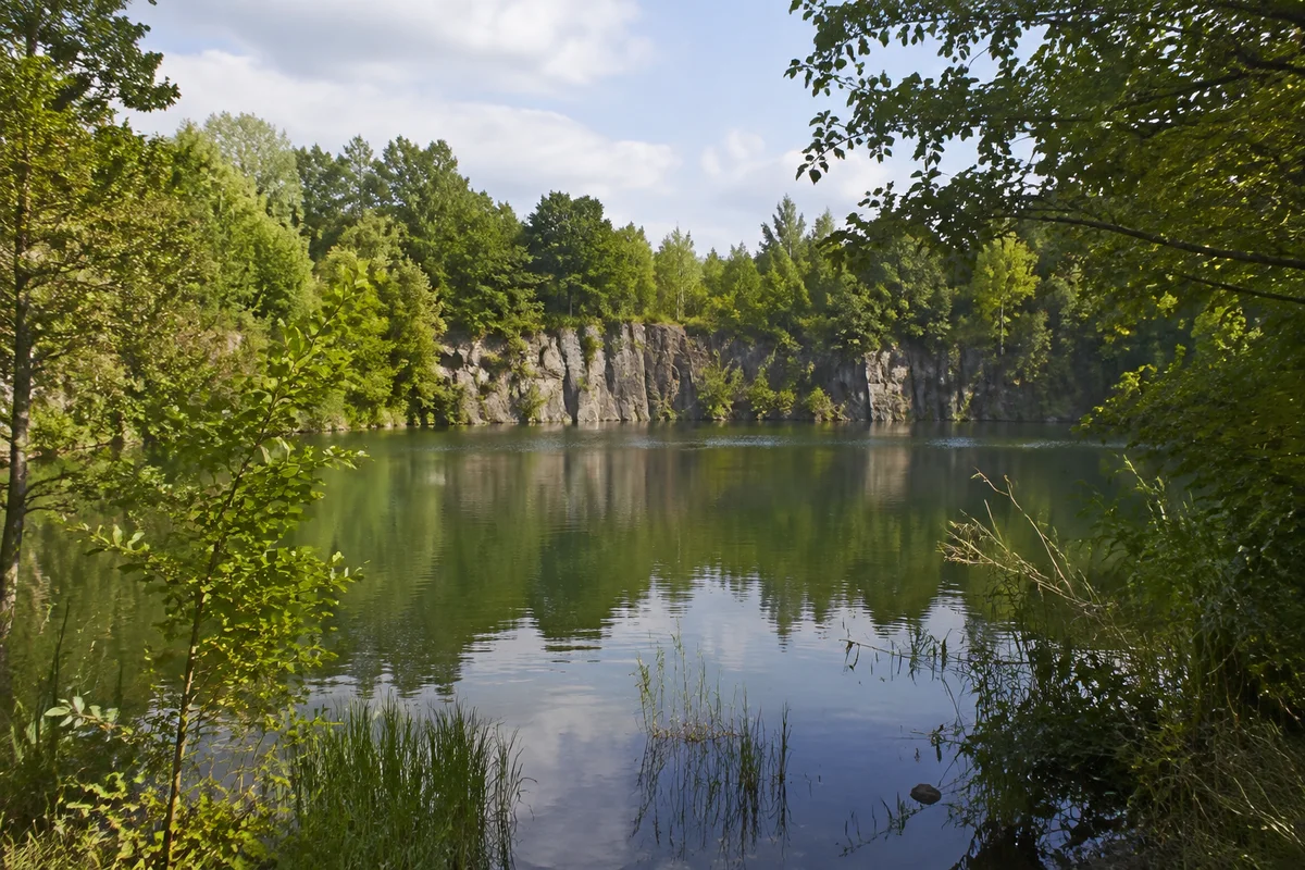Beucha: ruhiges ehemaliges Steinbruchwasser mit niedrigen grauen Felswänden und dichtem Grün, ohne Gebäude