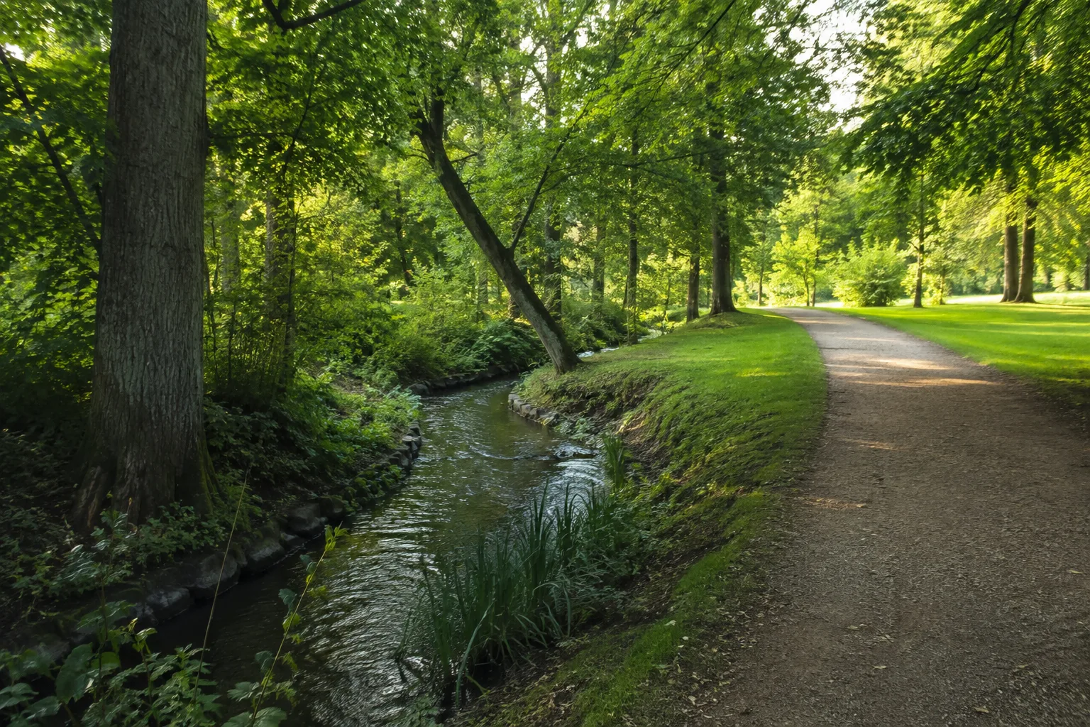 Stobber im Buckower Kurpark: schmaler Bach unter Laubbäumen neben einem gepflegten Parkweg