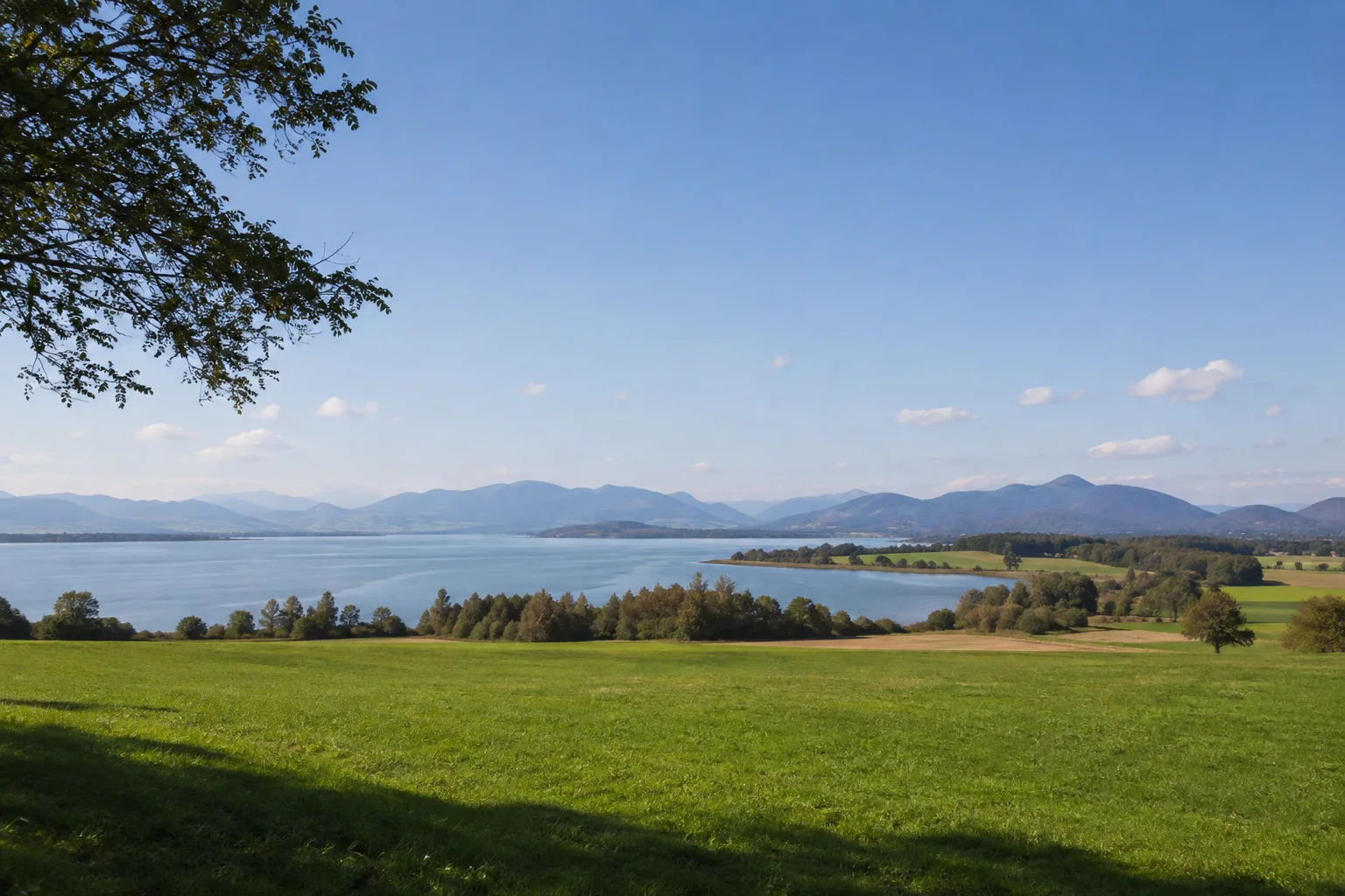 Ising am Chiemsee: sanfte Wiesen und Gehölze über einer breiten flachen Seebucht