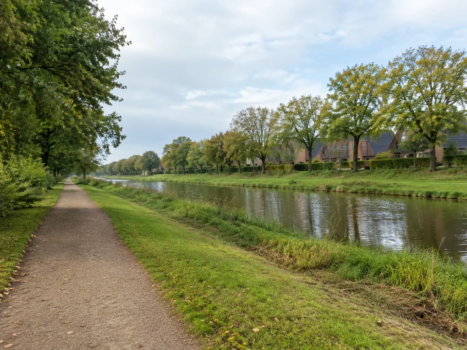 Emden: Gepflegter öffentlicher Weg neben einem geraden Kanal, niedrige Backsteinhäuser im Hintergrund und Bäume
