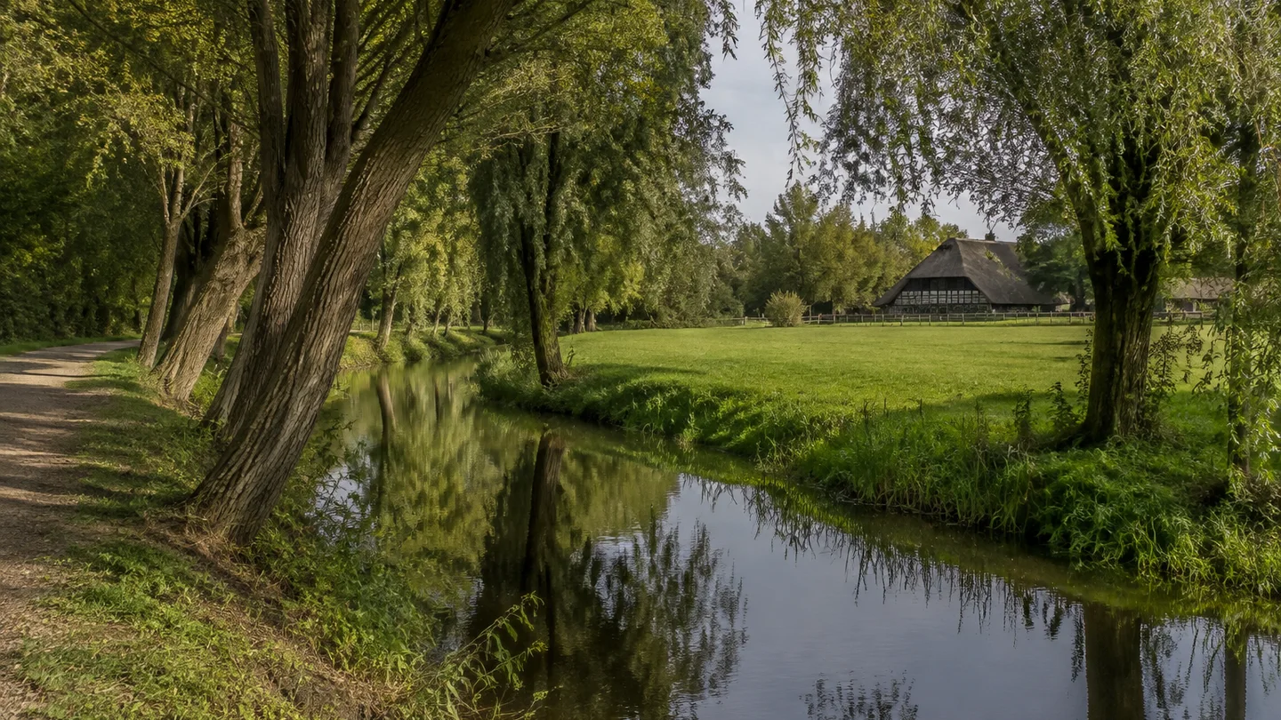 Fischerhude: Dorfkern an den Wümmearmen: Schmaler natürlicher Flussarm unter alten Eichen und Weiden zwischen grünen Wiesen, entfernt ein niedriges reetgedecktes Fachwerkbauernhaus