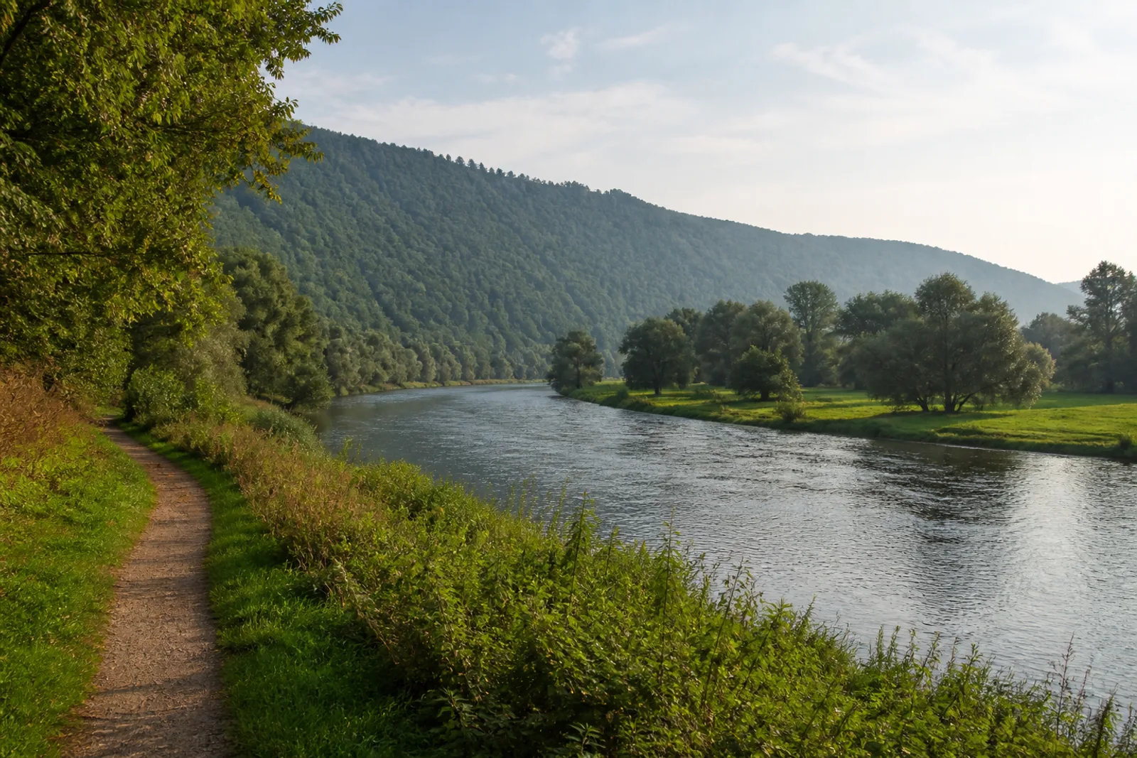 Uferweg an der Weser zwischen Wiesen und bewaldeten Höhen bei Höxter