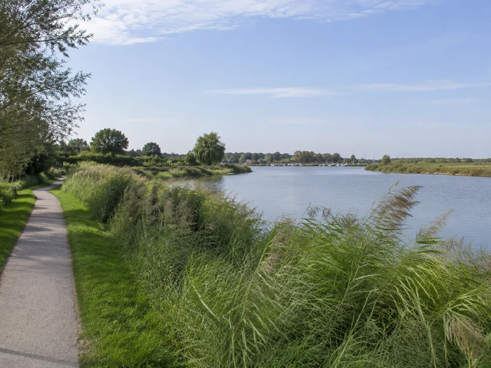 Krummhörn: Ruhiges Sieltief am Dorfrand mit Schilf und niedrigen Gärten, Kutterhafen nur fern im Hintergrund
