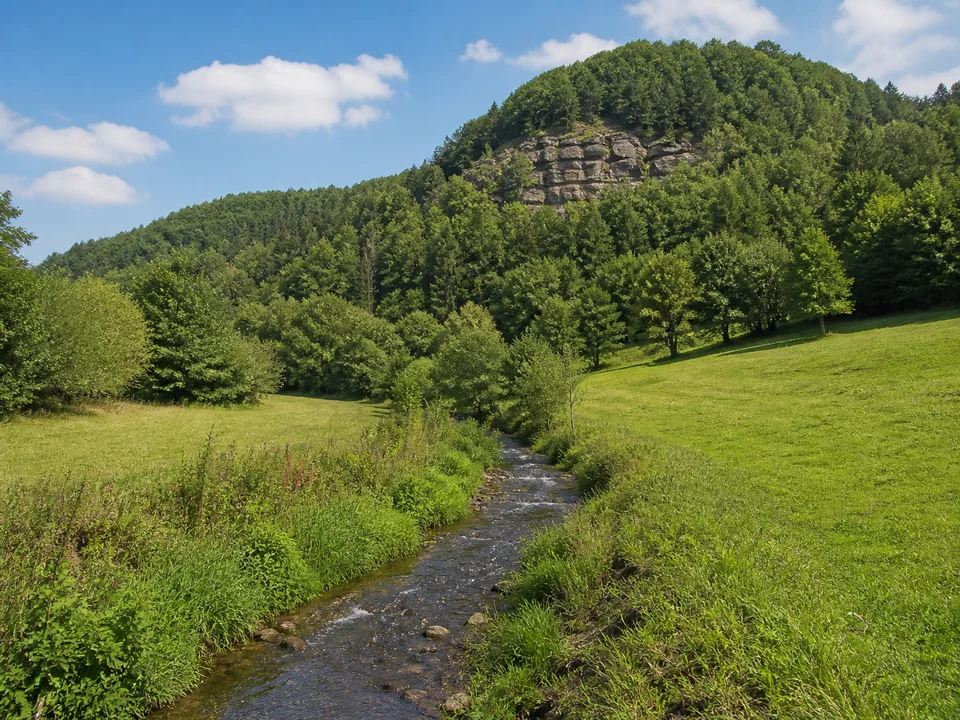 Lautertal bei Spiegelberg: Kleiner Bach zwischen grünen Wiesen unter bewaldeten runden Sandsteinhängen