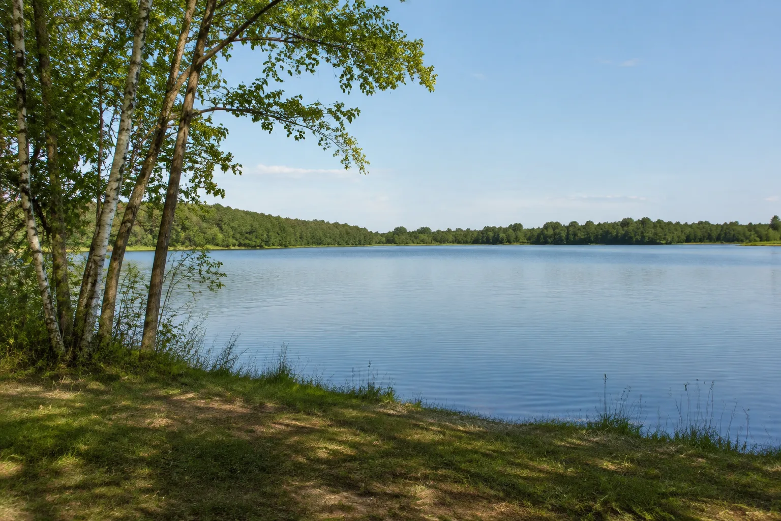Hindenberger See: offene Wasserfläche mit niedrigen bewaldeten Ufern und dörflichem Umfeld