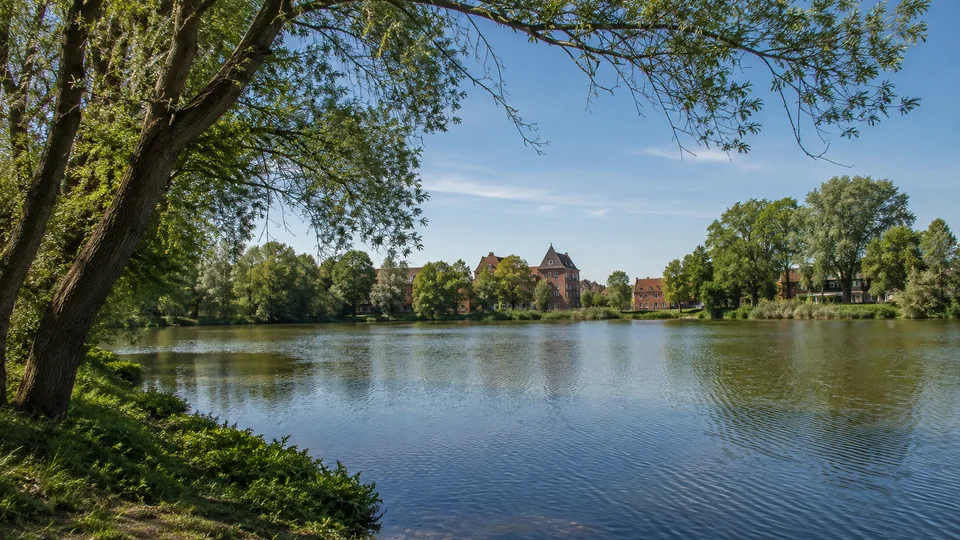 Möllner Stadtufer: Ruhiges Wasser am städtischen Ziegelsee mit Uferbäumen und zurückhaltender Backsteinbebauung in der Ferne