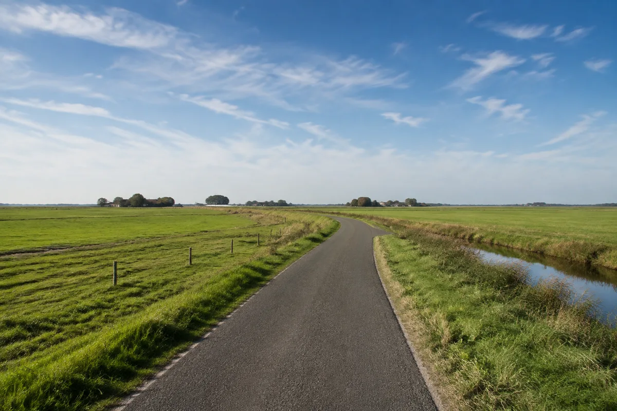 Pellworm Binnenwege: Schmale befestigte Inselstraße zwischen ebenen Weiden mit einzelnen niedrigen Höfen in der Ferne
